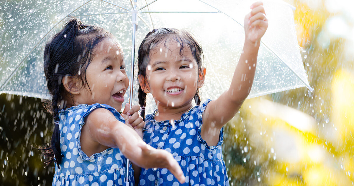 Two happy asian little girls with umbrella having fun to play with the rain together